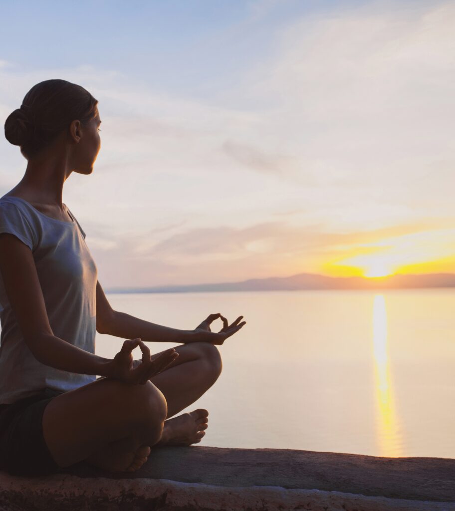 Kvinne mediterer i solnedgang ved havet